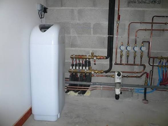 Adoucisseur d'eau blanc raccordé aux nourrices de distribution et aux compteurs dans un local technique