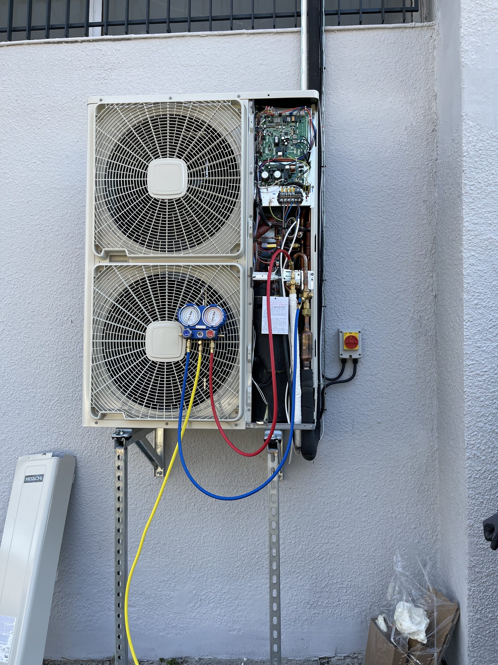 Groupe extérieur de climatisation Hitachi fixé en façade sur consoles, manomètres branchés pour la mise en service