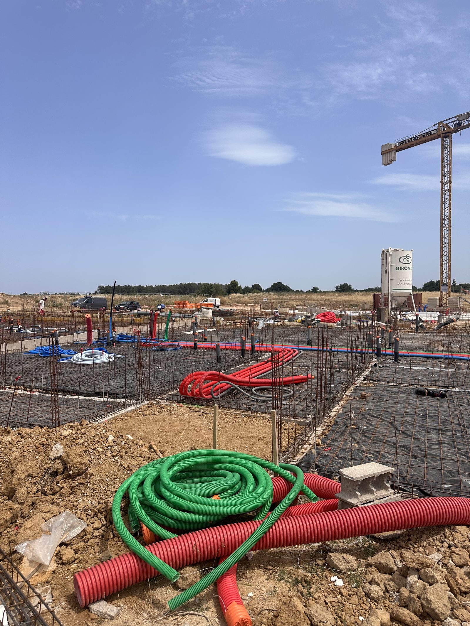 Plateforme de résidence en construction avec fourreaux rouges et verts et réseaux en attente, grue à tour en fond
